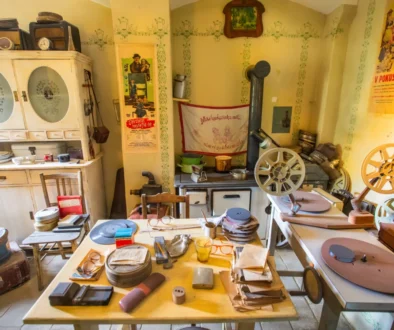 Cluttered vintage workshop with film reels, projectors, and wooden cabinets against yellow walls with retro posters and green trim patterns.