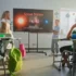 Teacher leads a solar system lesson as students sit at desks facing a large screen in a bright classroom.