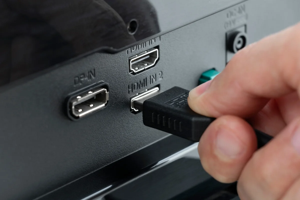 Detailní záběr osoby, která zasouvá konektor do HDMI vstupu s označením „HDMI IN 2“ na zadní straně elektronického zařízení.