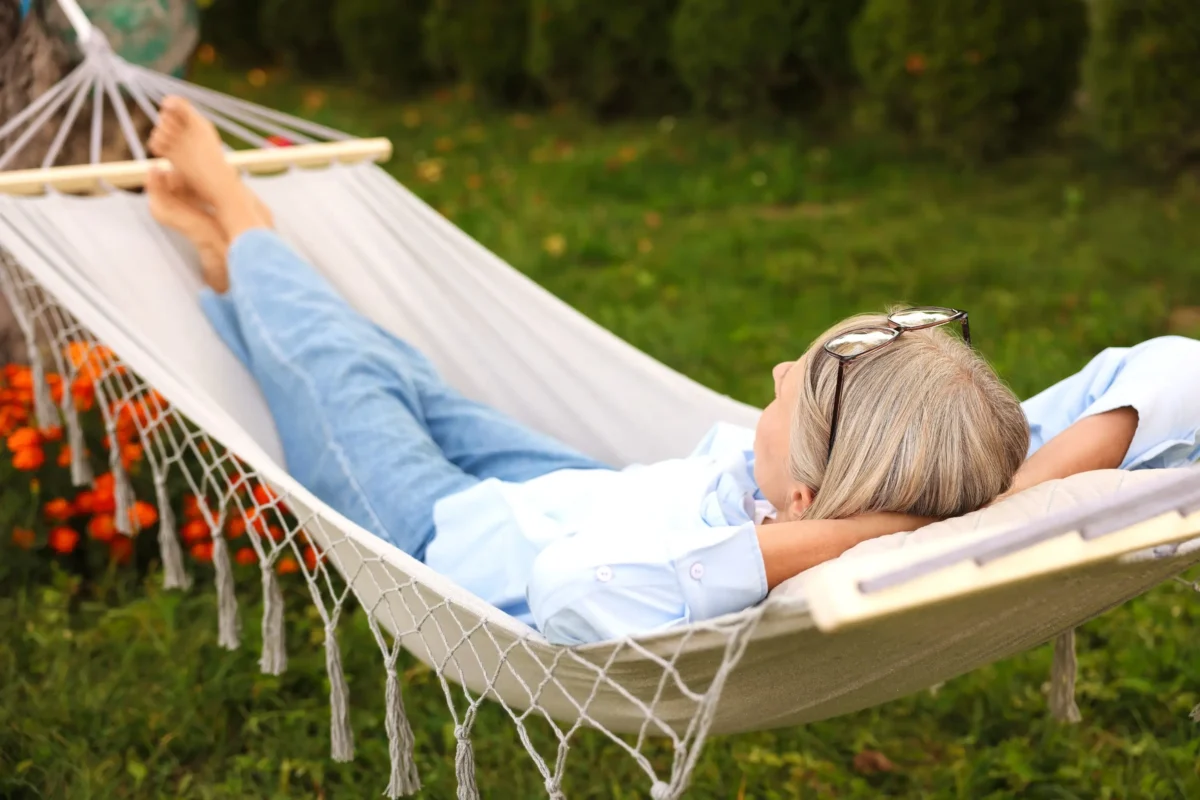 shutterstock_2690793103-změněno-na-3000x2001 | TVGURU.cz Osoba relaxující v bílé houpací síti venku, na sobě má světle modrou košili s brýlemi položenými na hlavě, nohy jsou ve vzduchu.