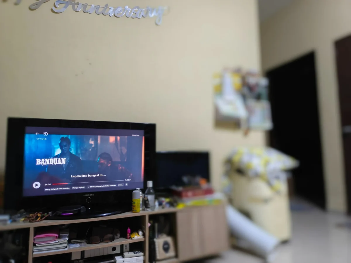 shutterstock_2752056873-změněno-na-3000x2250 | TVGURU.cz Rozmazaný obývací pokoj s počítačovým monitorem na dřevěném stole a přeplněnými policemi v pozadí; nahoře částečně viditelná nástěnná dekorace.