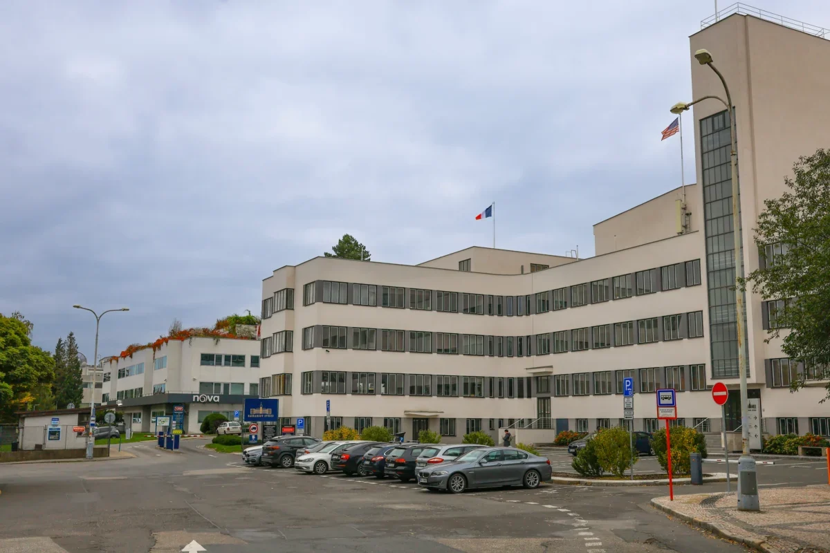 Modern white office building with many windows, two flagpoles (French and American) and a front parking lot under a cloudy sky.