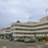 Modern white office building with many windows, two flagpoles (French and American) and a front parking lot under a cloudy sky.