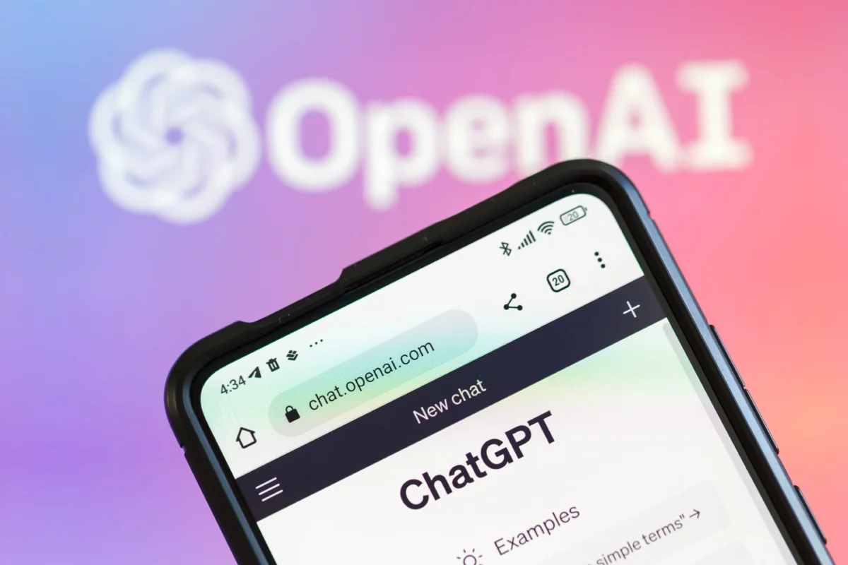 Smartphone screen showing the ChatGPT homepage (chat.openai.com) with a blurred OpenAI logo in a pink-to-purple gradient background behind it.