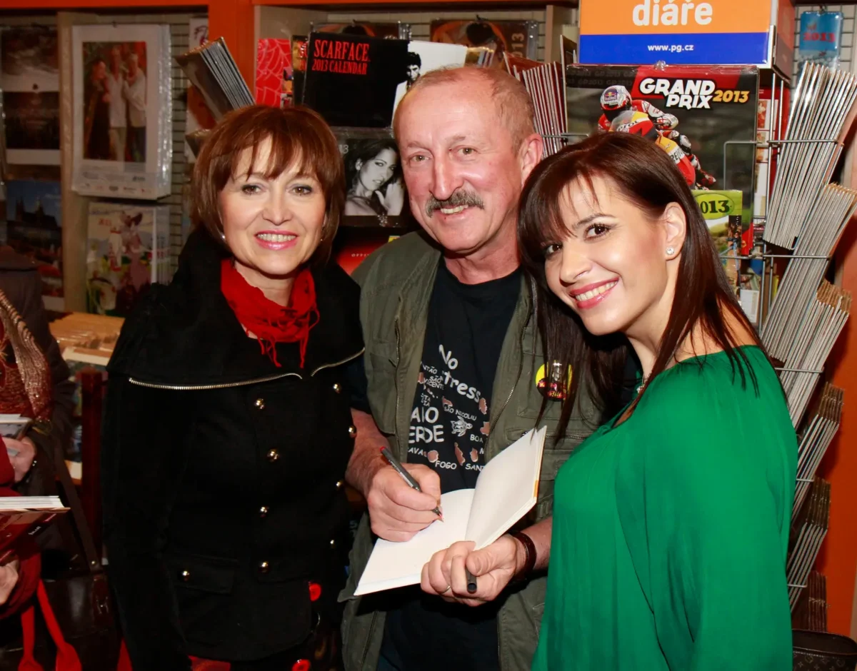 V pořadu se občas představí i známé osobnosti. Zdroj: Profimedia | TVGURU.cz Three people in a bookstore posing for a photo; the man in the center signs a notebook while two women smile.