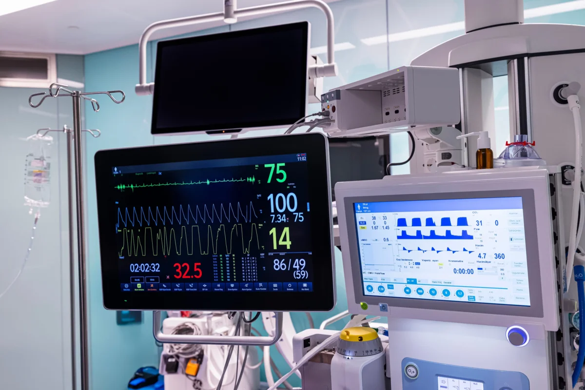 Intensive care monitors showing heart rate and vital signs with connected tubes and medical equipment nearby.