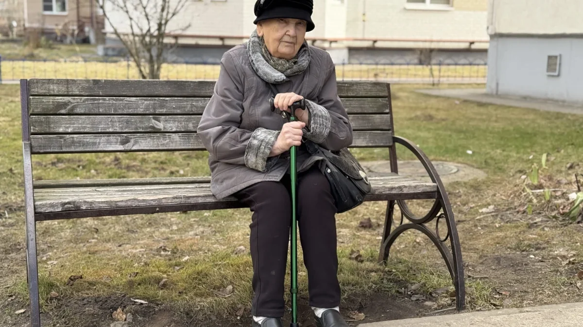 seniorka v klobouku s holí sedící na lavičce