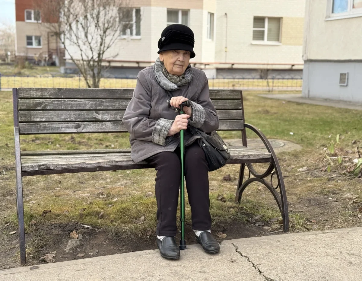 seniorka v klobouku s holí sedící na lavičce
