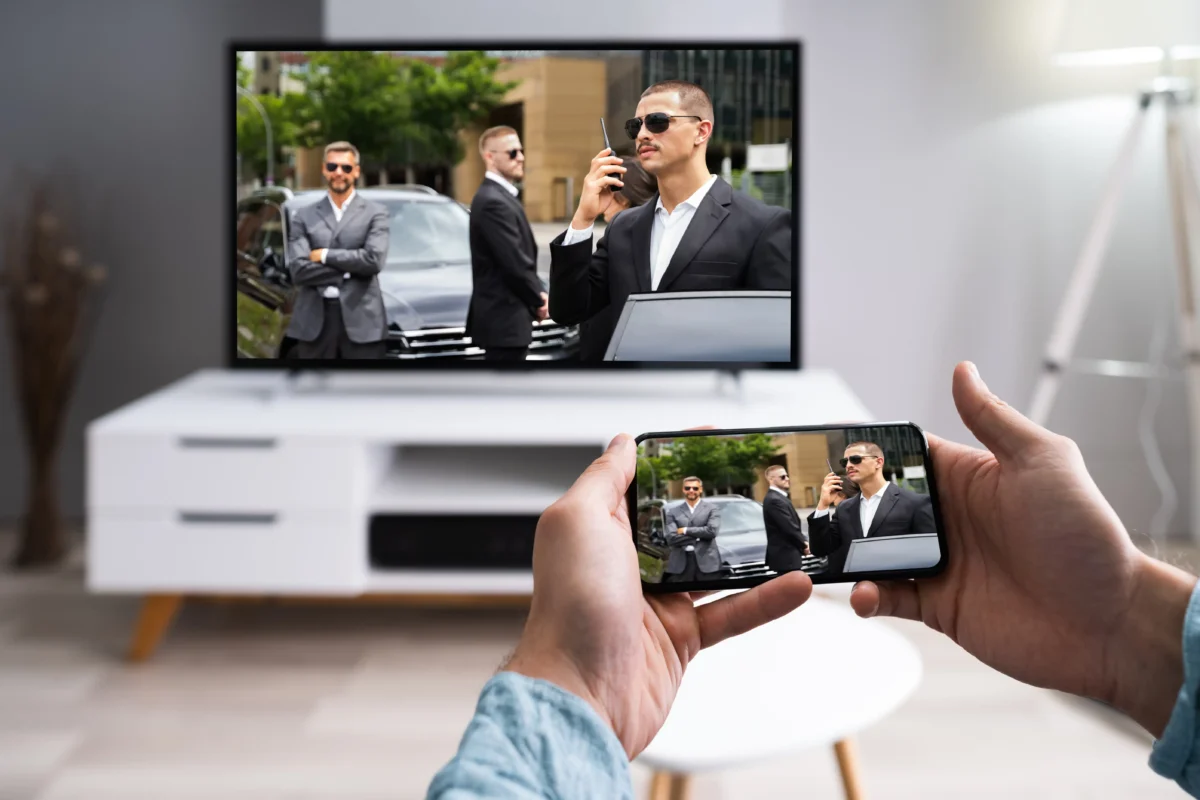 Televizi lze v dnešní době sledovat i na telefonu. Zdroj: Shutterstock | TVGURU.cz Ruce držící telefon s filmem a televize v pozadí