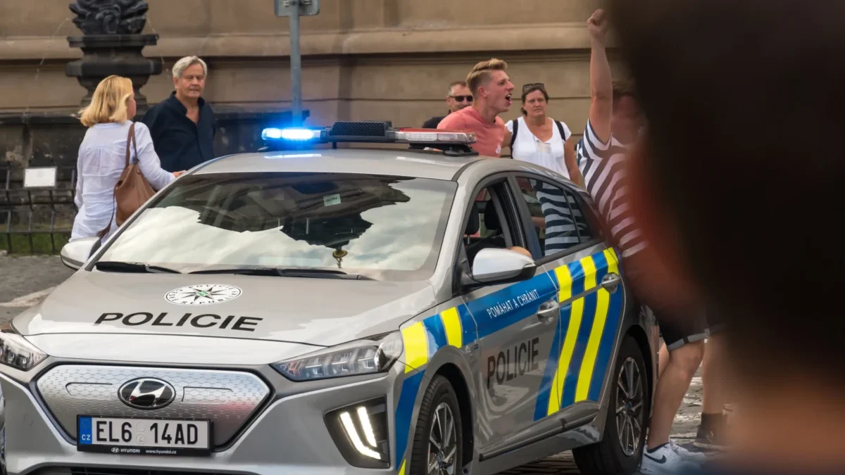 Lidé postávají u policejního auta.