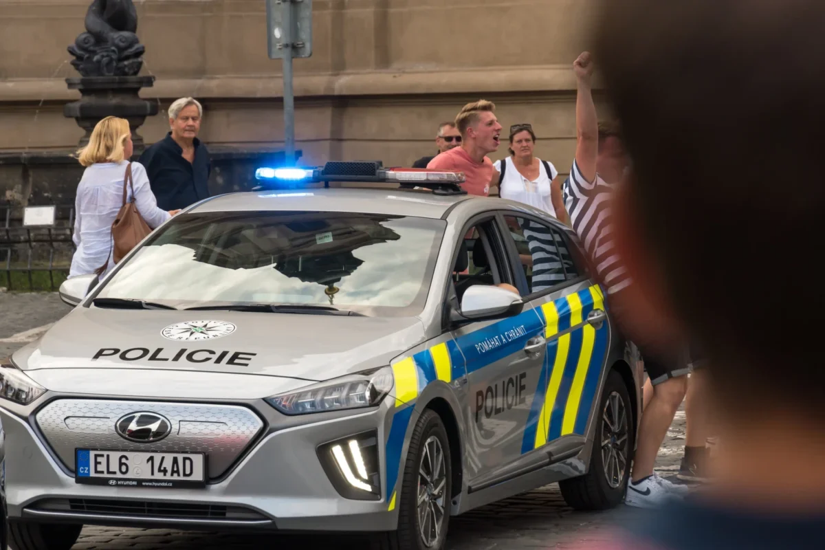 Lidé postávají u policejního auta.