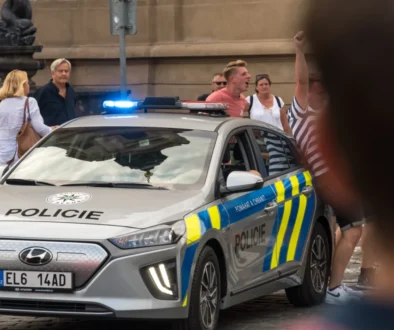 Lidé postávají u policejního auta.