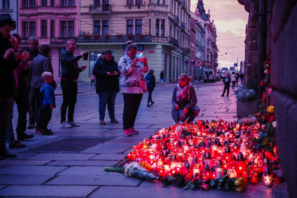 Lidé se za soumraku shromažďují na městské ulici a obklopují dlouhou řadu zapálených červených svíček na počest nebo na vigilii.