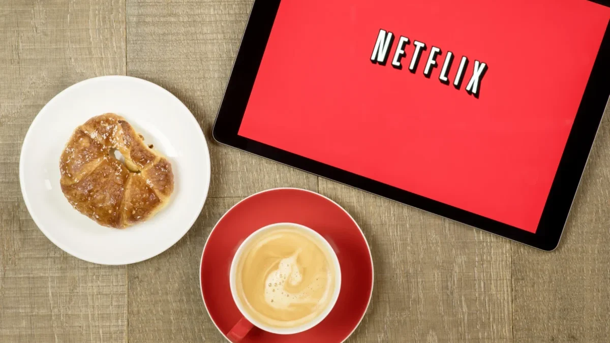 Na tabletu je puštěný Netflix a vedle leží svačina s kávou.