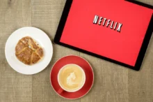 Na tabletu je puštěný Netflix a vedle leží svačina s kávou.