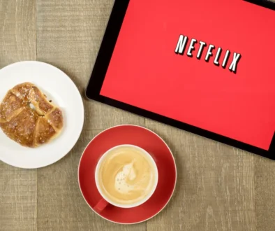 Na tabletu je puštěný Netflix a vedle leží svačina s kávou.