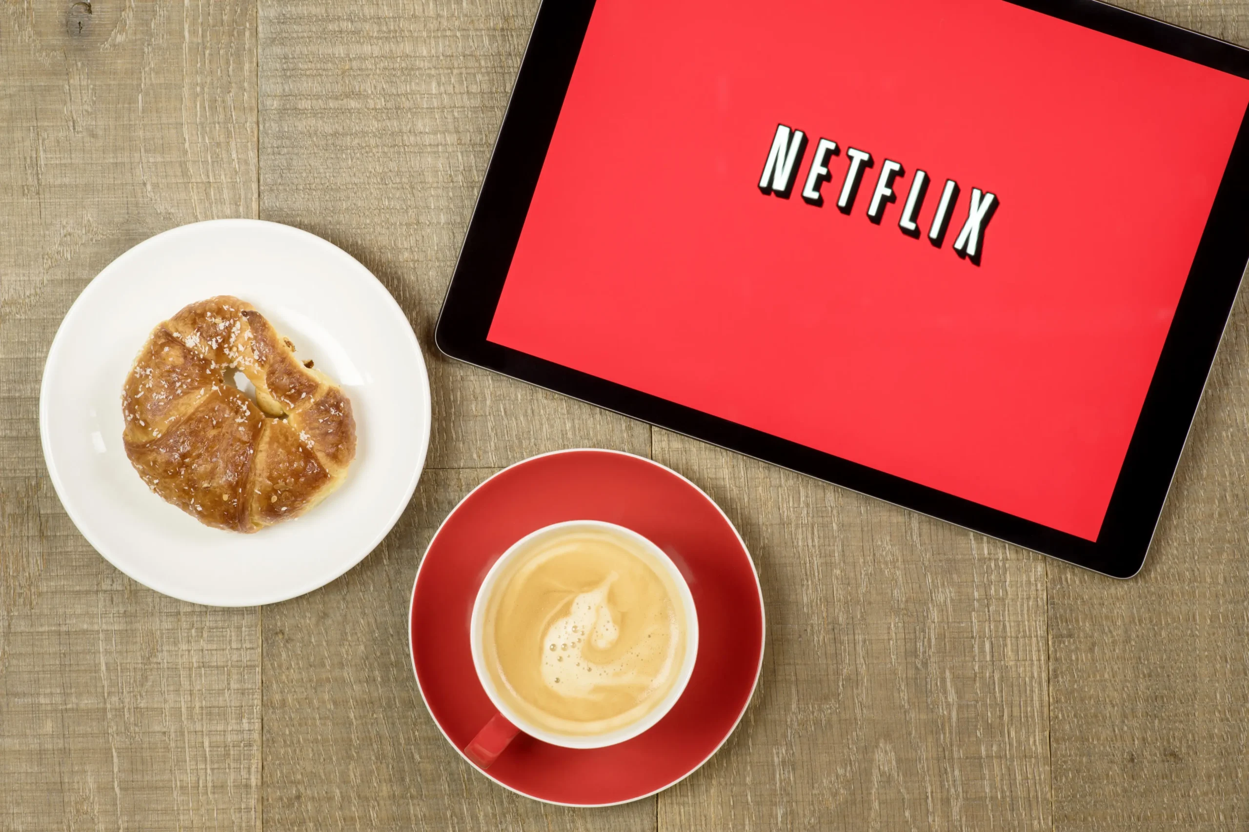 Na tabletu je puštěný Netflix a vedle leží svačina s kávou.