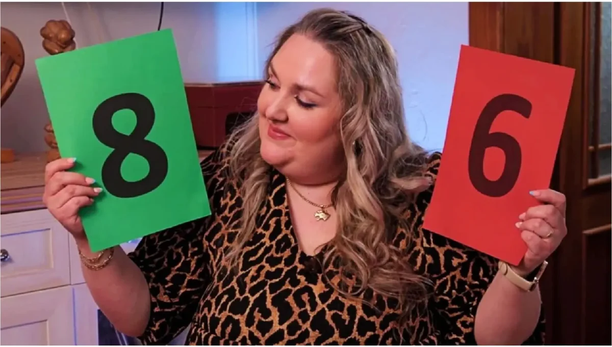 prostřeno 1 | TVGURU.cz Woman in a leopard-print blouse holds a green card with 8 and a red card with 6, looking at the 8 card.