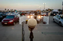 Close-up of a microphone on a stand in the foreground with a blurred outdoor parking lot full of cars in the background.