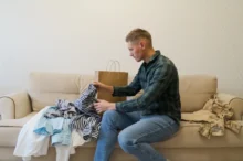 Muž na gauči rozbalující nové oblečení.
