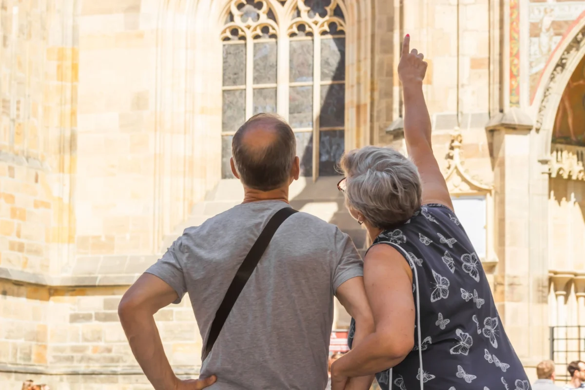 shutterstock_2186949099 1 | TVGURU.cz Two people stand with backs to the camera, looking at a historic stone building, one raising a finger toward the architectural details nearby.