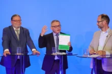 Tři muži v oblecích u moderovacích pultíků