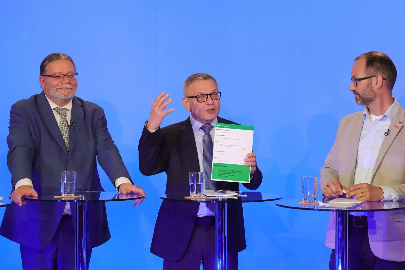 Tři muži v oblecích u moderovacích pultíků