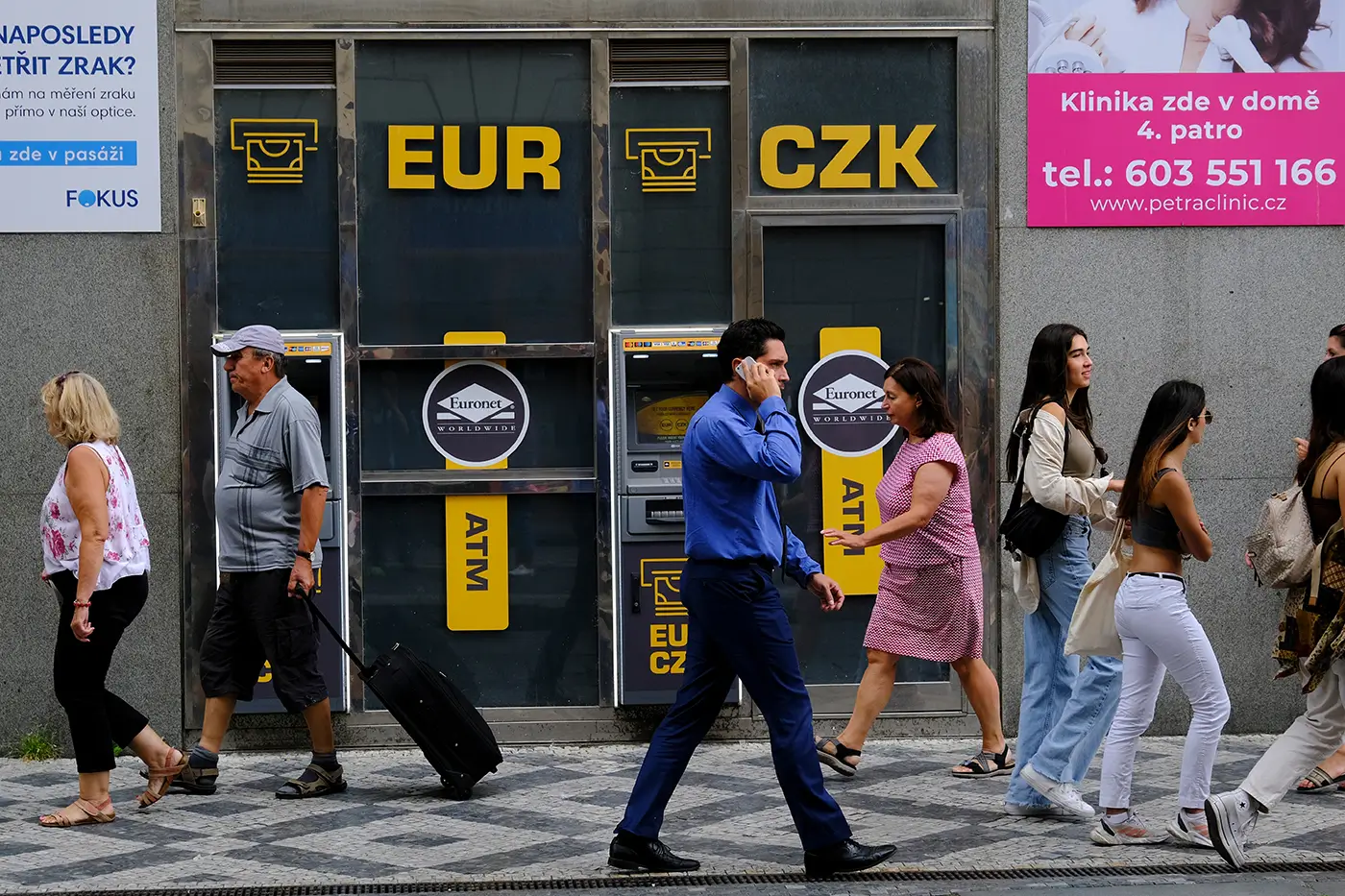 Lidé chodí po ulici kolem bankomatu
