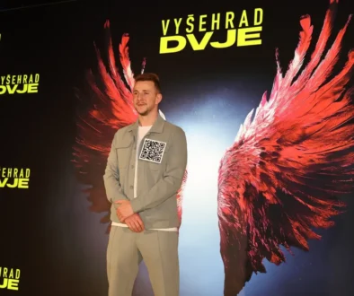 Muž stojí před filmovým plakátem, na kterém jsou vyobrazená červená křídla