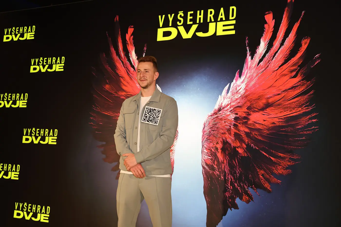 Muž stojí před filmovým plakátem, na kterém jsou vyobrazená červená křídla