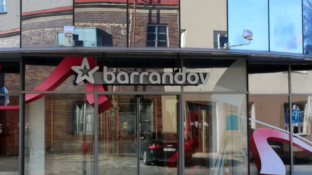 Storefront window with the 'Barrandov' sign and a white star logo, reflecting brick buildings across the street.