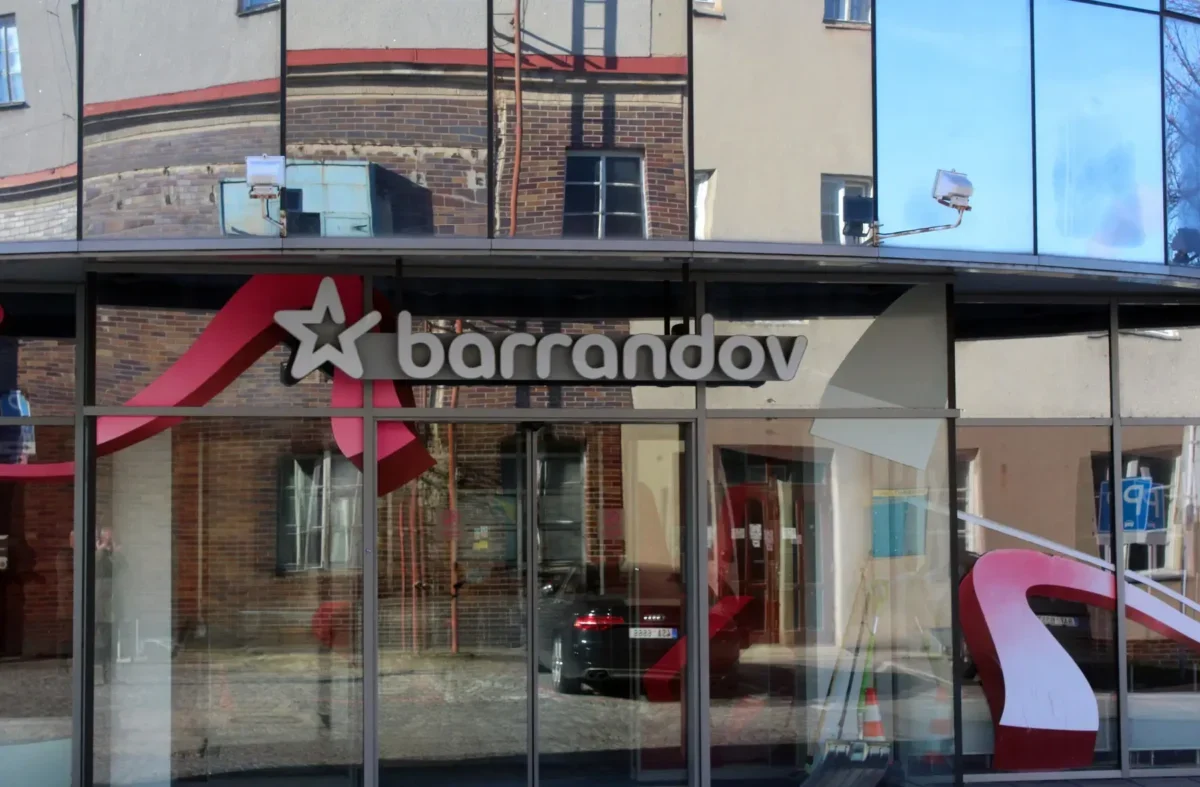 Storefront window with the 'Barrandov' sign and a white star logo, reflecting brick buildings across the street.