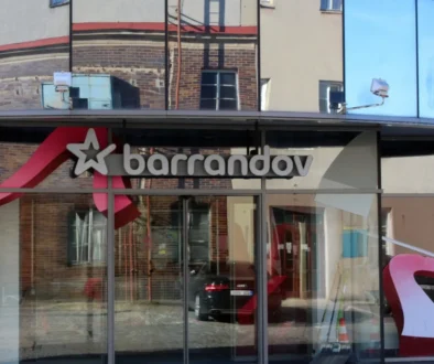 Storefront window with the 'Barrandov' sign and a white star logo, reflecting brick buildings across the street.