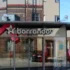 Storefront window with the 'Barrandov' sign and a white star logo, reflecting brick buildings across the street.