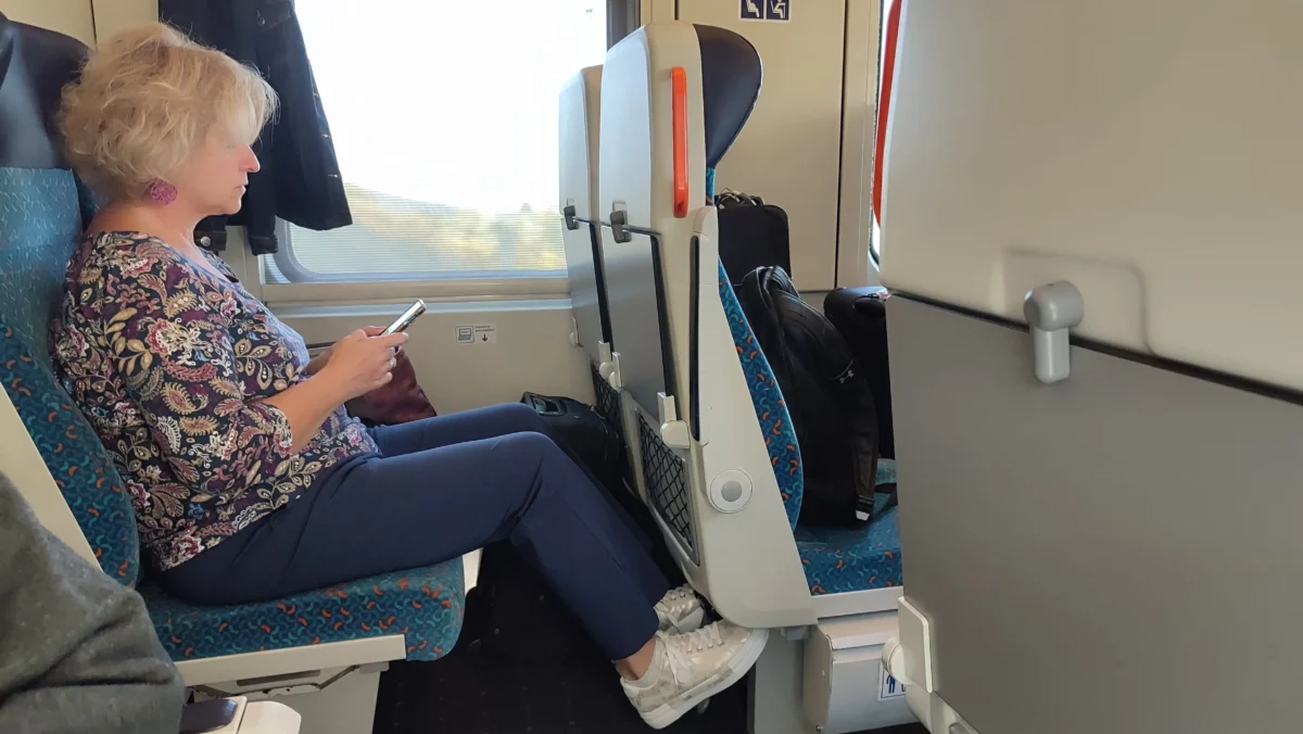shutterstock_2587018187 1 | TVGURU.cz Woman with short blonde hair sits on a blue patterned train seat, focused on a smartphone she’s holding.