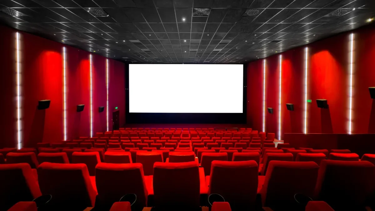 Red-walled cinema interior with a large white screen at the front and red seating throughout the auditorium.