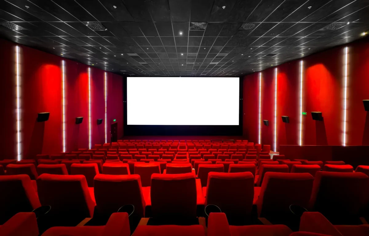 Red-walled cinema interior with a large white screen at the front and red seating throughout the auditorium.
