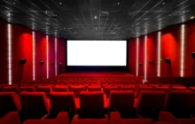 Red-walled cinema interior with a large white screen at the front and red seating throughout the auditorium.