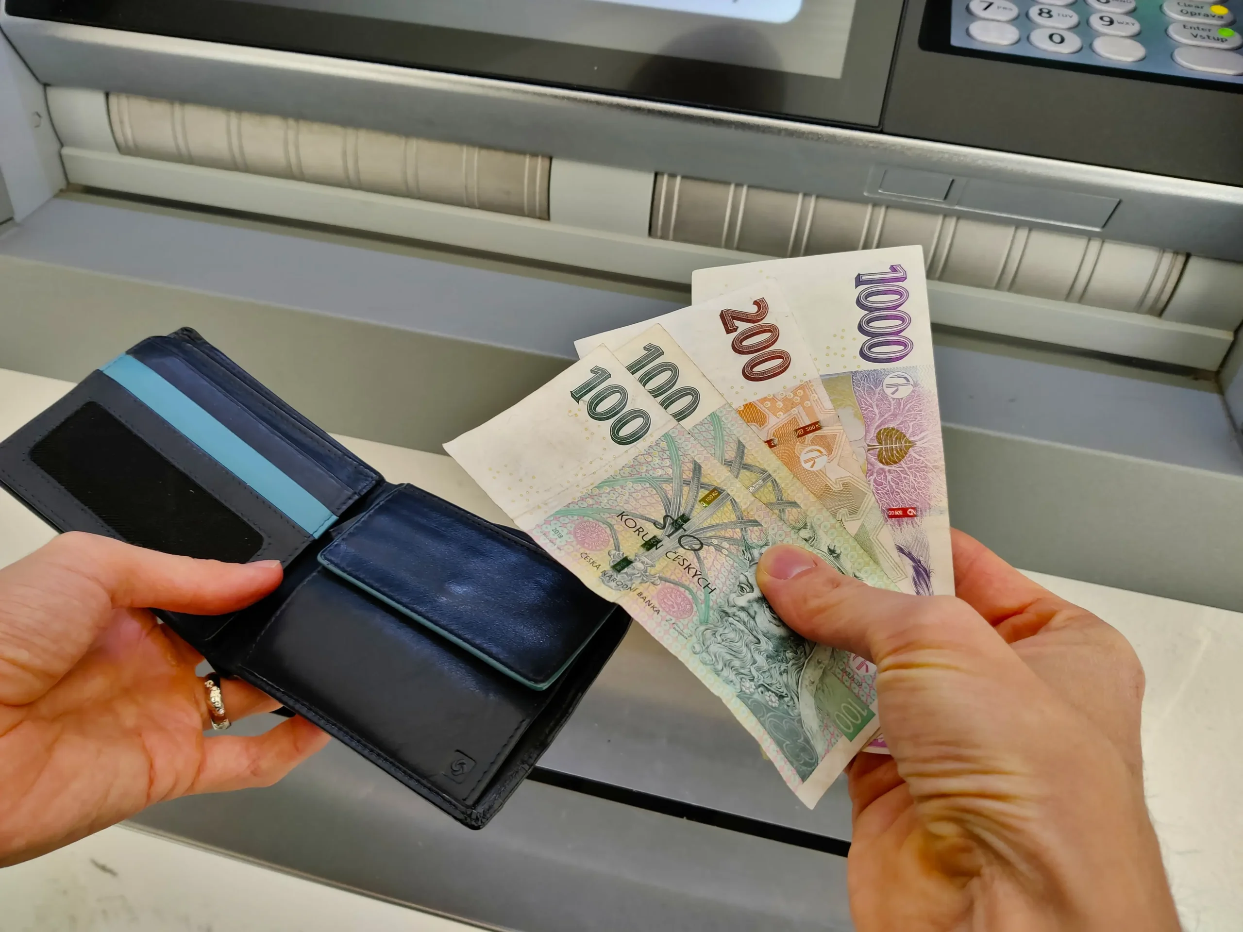 České bankovky v ruce u bankomatu