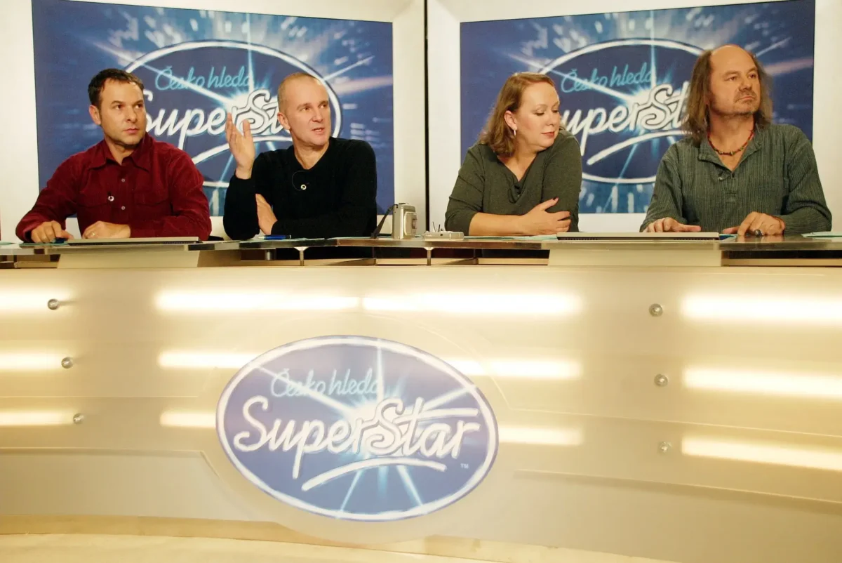 profimedia-0219445168 1 | TVGURU.cz Four judges sit behind a glossy panel with a blue'SuperStar' logo backdrop, looking attentive or talking among themselves.