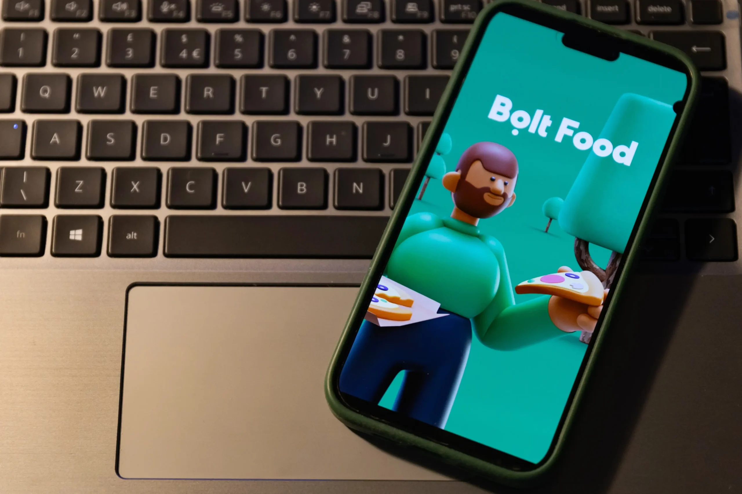 Aplikace Bolt Food na mobilním telefonu v pozadí s notebookem