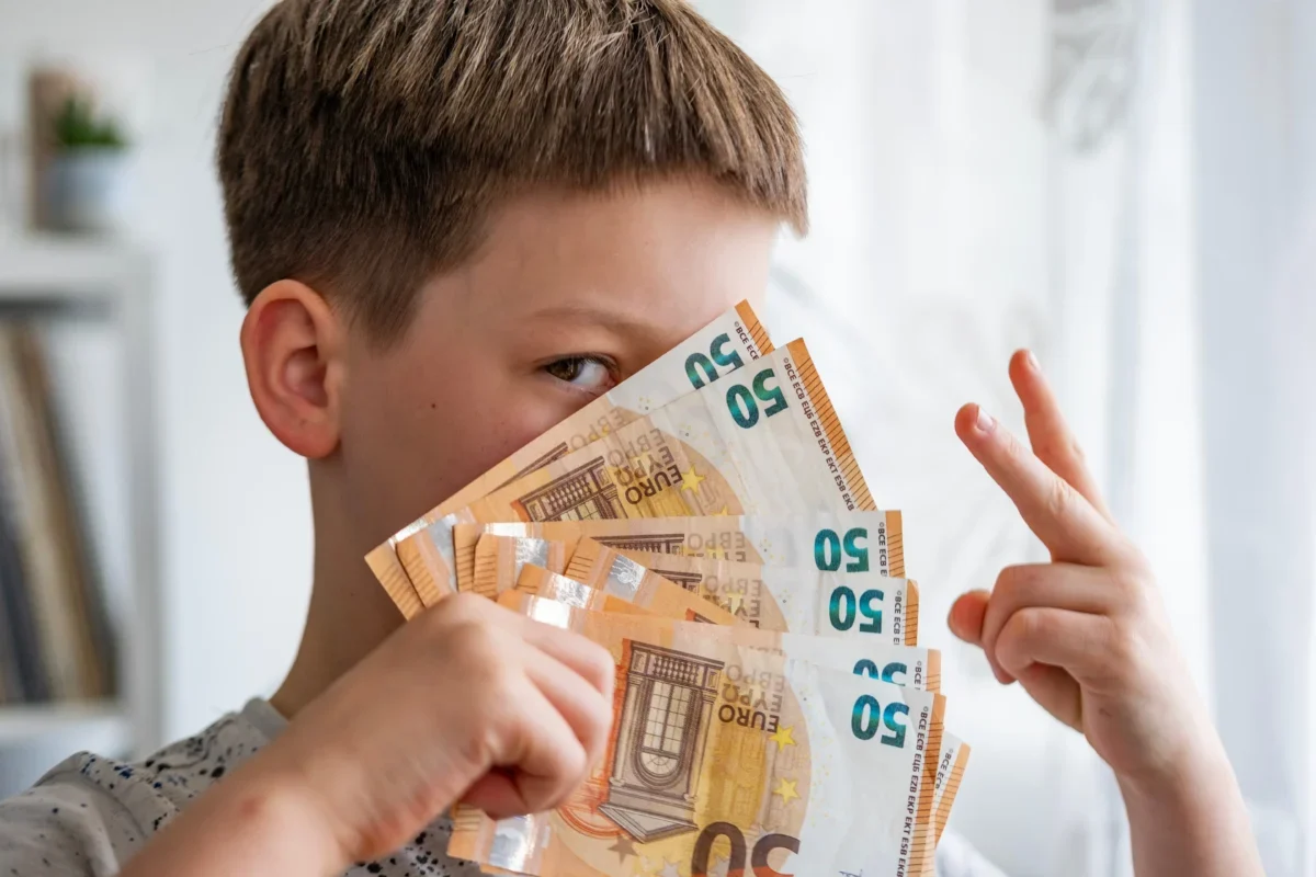 Chlapec drží vějíř eurových bankovek před obličejem