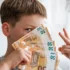 Chlapec drží vějíř eurových bankovek před obličejem