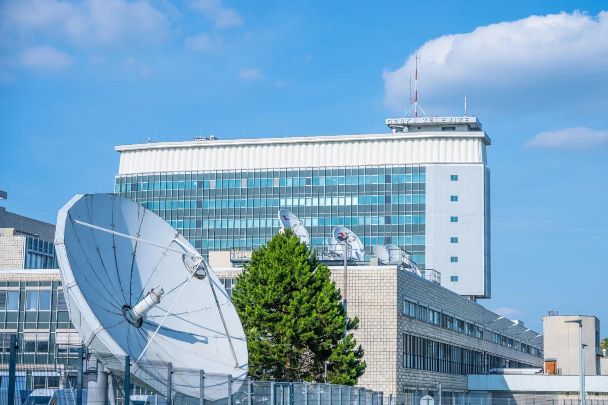Moderní kancelářské budovy s obrovským satelitem v popředí na pozadí modrého nebe.