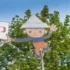 Whimsical cartoon boy cutout hanging from a pole among green trees against a blue sky, with a sign to the left.
