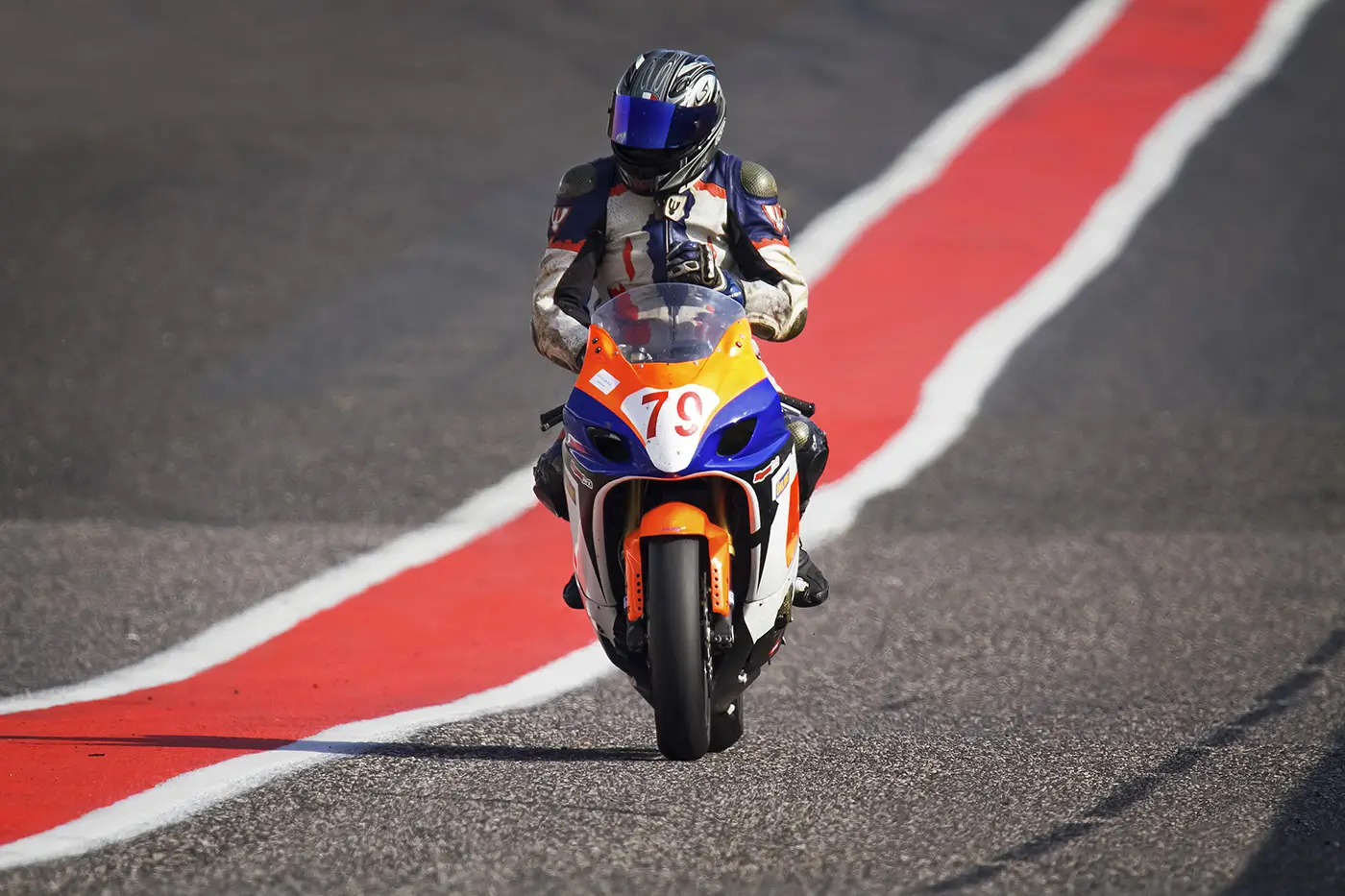 Na závodní dráze jede člověk v motorkářské výstroji na závodní motorce
