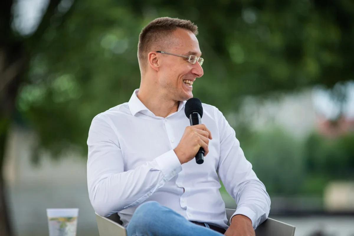 Muž v bílé košili a riflích mluví do mikrofonu.