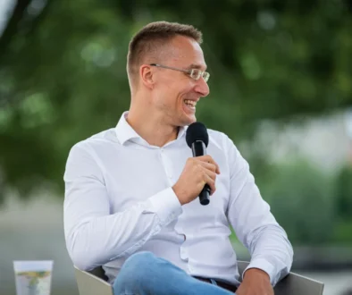 Muž v bílé košili a riflích mluví do mikrofonu.