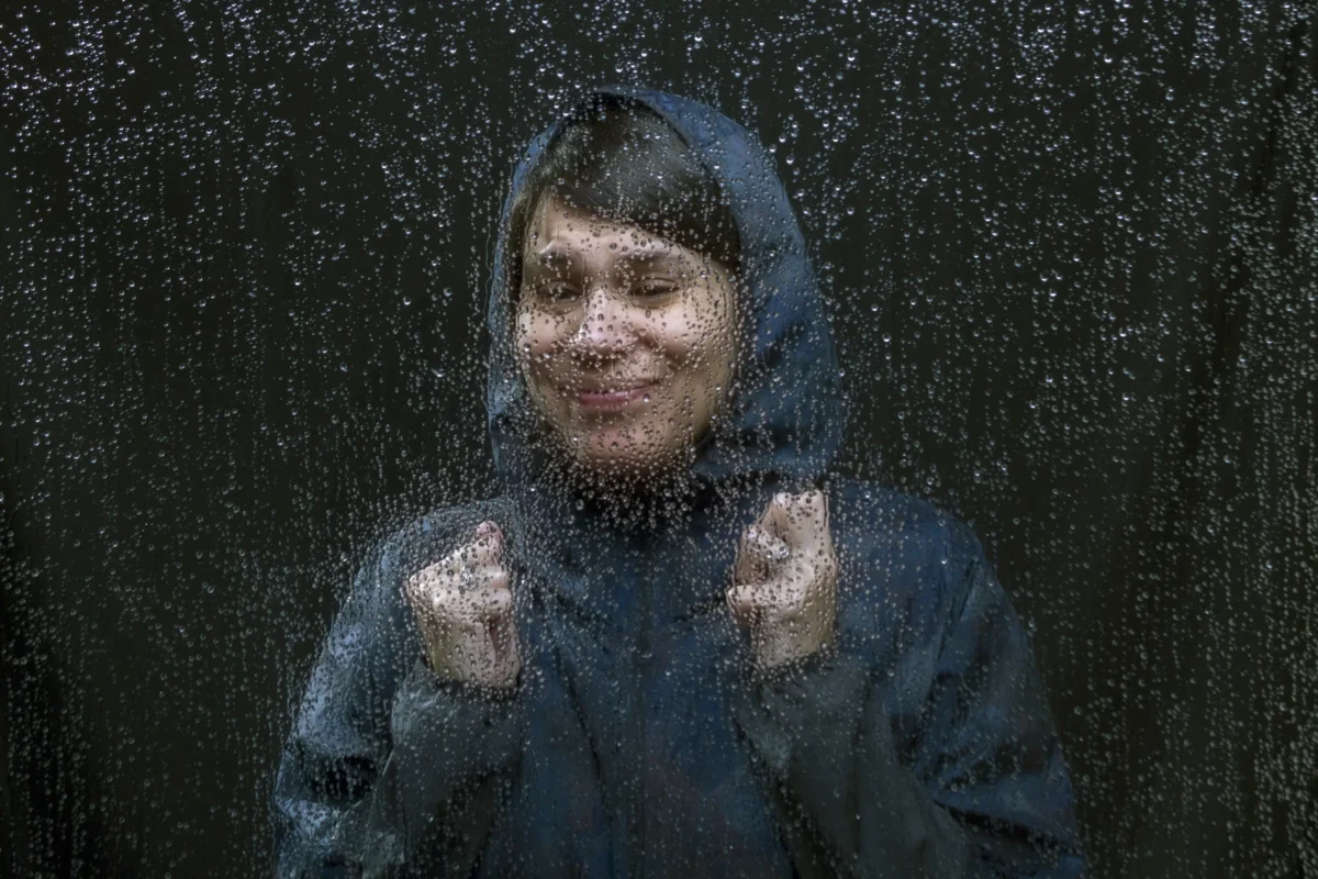 shutterstock_716298622-2 | TVGURU.cz Žena stojí za oknem, na kterém jsou kapky vody.