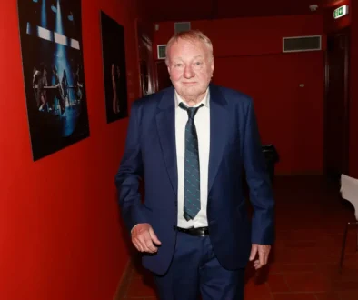 Muž v saku, kravatě a bílé košili stojí na chodbě s červenými stěnami